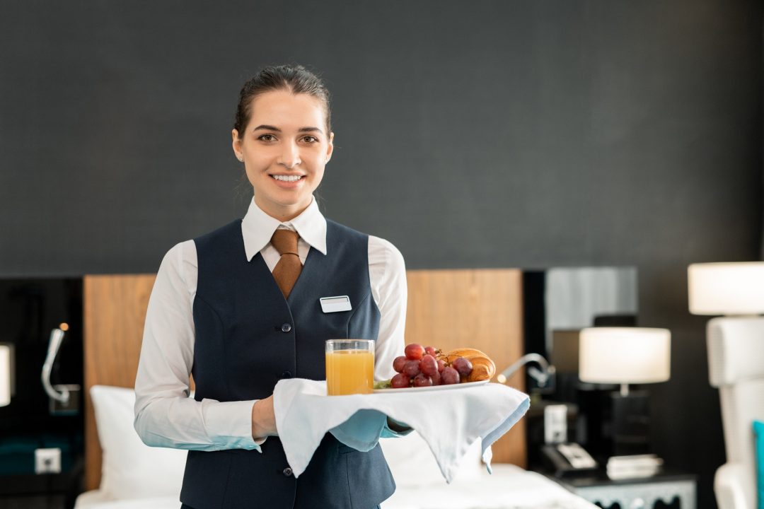 young smiling hotel staff holding tray with breakfast.jpg